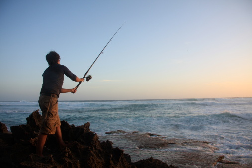 A young man fishing on rocks at sunset. (Denmark, Western Australia)