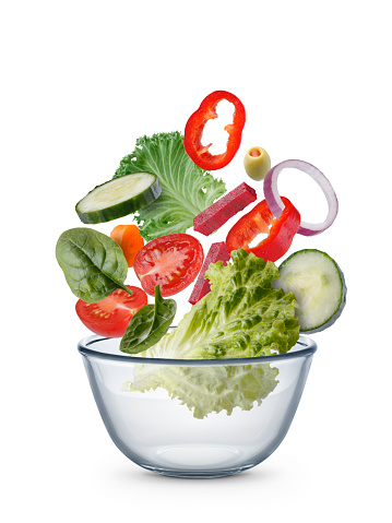 Salad ingredients flying through the air, landing in a bowl