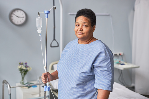 Waist up portrait of black senior woman looking at camera in hospital room with IV