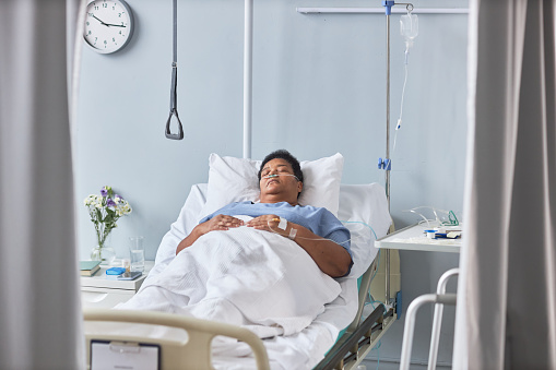 Portrait of senior female patient sleeping on bed in hospital room with tubes and IV support
