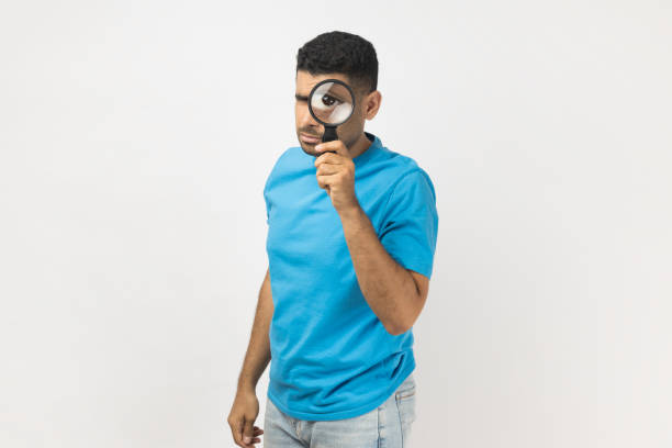 istock Man standing holding magnifying glass and looking at camera with big zoom eye verifying authenticity 1469544774