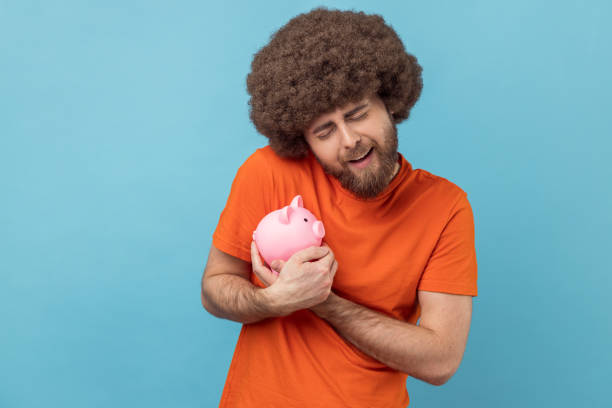 süßer mann, der sparschwein hält und umarmt, gibt sein geld niemandem. - piggy bank savings wealth coin bank stock-fotos und bilder