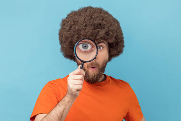 istock Man standing, holding magnifying glass and looking at camera with big zoom eye. 1469546423