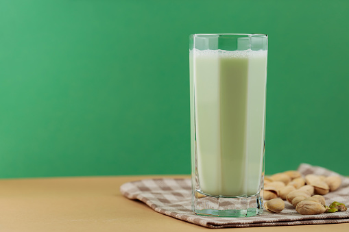 Organic non dairy pistachio milk in glass. Vegan pistachio milk and pistachios on a beige green background