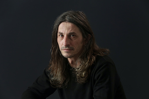 Portrait of middle aged man with long hair on black background