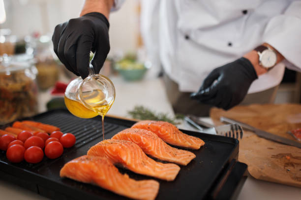 primer plano de un chef irreconocible vertiendo aceite sobre salmón en parrilla eléctrica - prepared fish fish grilled close up fotografías e imágenes de stock