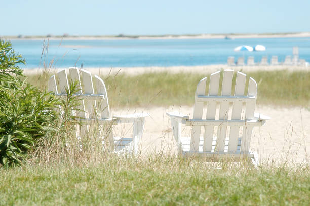Two white Adirondack chairs near the shore white adirondack chairs, cape cod, beach, ocean, natural beach cape cod photos stock pictures, royalty-free photos & images
