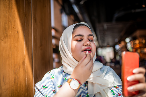 Portrait of a Muslim teenager putting red lipstick on.