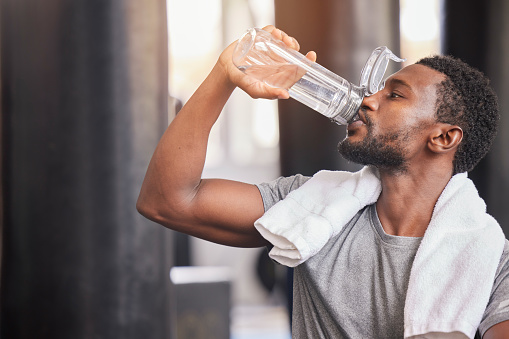 Fitness, drinking water and relax with black man in gym for training, endurance and workout. Energy, focus and sweat with athlete bodybuilder cooling down in club for sports, exercise and cardio