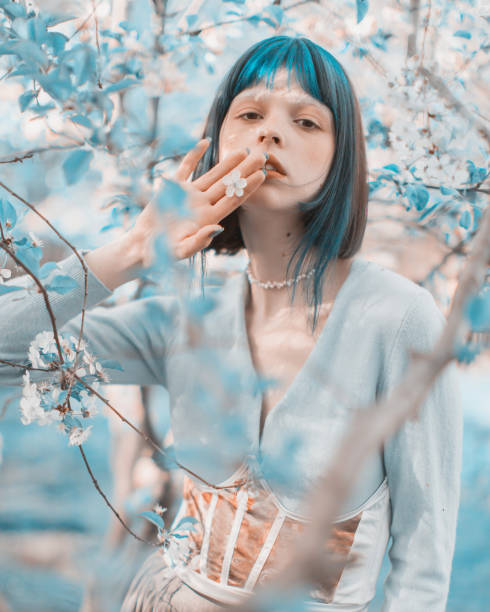 Asian woman with blue hair on the background of a flowering tree. Bang hairstyle. Spring garden. White flowers stock photo