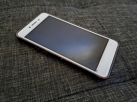 Smart phone with blank screen isolated on a gray textured background. White mobile phone with black screen