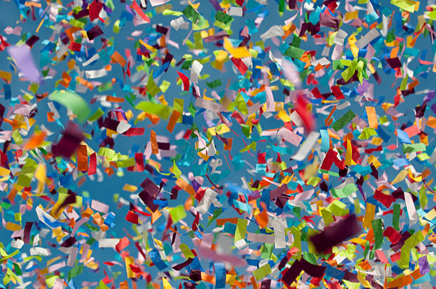 Multicolor confetti falling in blue sky background, low angle view