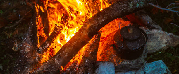 istock Boiling of tea in kettle on bonfire with large firewood. Tea drinking in open air. Active outdoor recreation. Camping in dusk. Romantic warm atmosphere in twilight on nature. Active rest. 1469602611