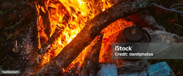 istock Boiling of tea in kettle on bonfire with large firewood. Tea drinking in open air. Active outdoor recreation. Camping in dusk. Romantic warm atmosphere in twilight on nature. Active rest. 1469602611