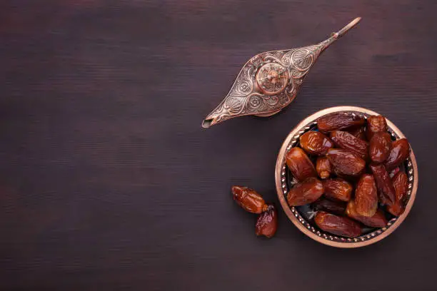 Plate with dates  and aladdin lamp on dark brown painted wooden background  with empty space for text . Flat lay. Ramadan background.