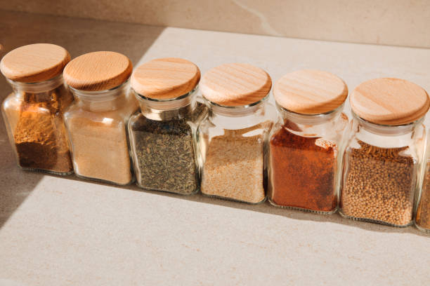 A group of seasoning in glass jars on a light stone background. Paprika, herbs, mustard, garlic, front view, selective focus stock photo