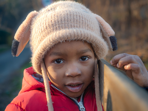 Portrait of African little kid in warm outerwear colorful vest and knit beanie cap with earflaps, p children's fashion clothing and fashion outdoors