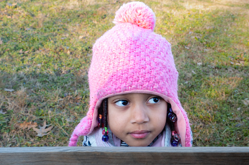 cute smiling african american baby girl in white outfit outdoors at sunset wearing a pink beanie knit hat with earflaps