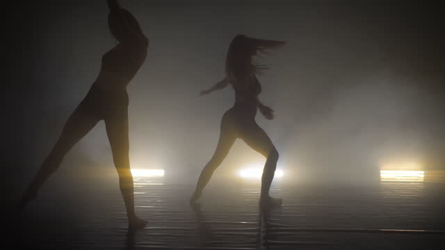 Two young women training their styles of dancing in the smoky studio