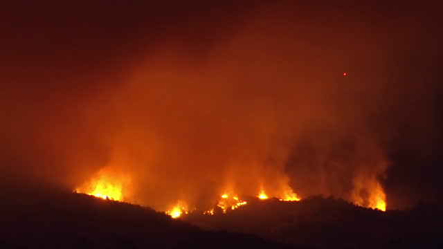 Hill with trees about to burn in red, orange wildfire glowing at night