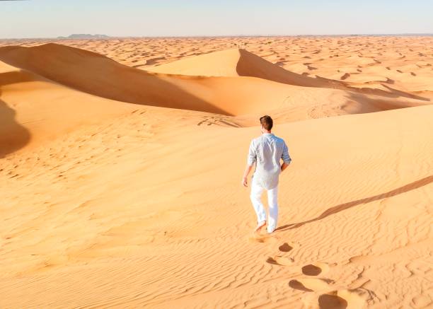 junge männer zu fuß in der wüste von dubai, sanddünen von dubai vereinigte arabische emirate - dubai united arab emirates traditional culture camel stock-fotos und bilder
