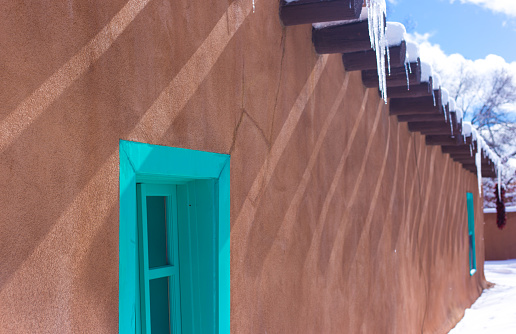 Santa Fe, NM: Old Adobe House in winter, with turquoise window and icicles. Copy space available. House built in the 1800s.