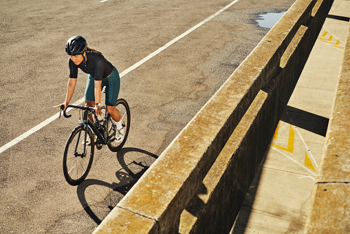 Bike, asphalt and mockup with a woman cycling on a city brige for cardio or endurance exercise. Bicycle, street and fitness with a female cyclist or athlete riding outdoor on an urban background