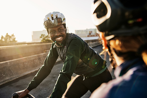 Fitness, cycling and smile with black man in city for sports, health and workout. Training, teamwork and wellness with friends riding bikes in urban town for relax, motivation and cardio adventure
