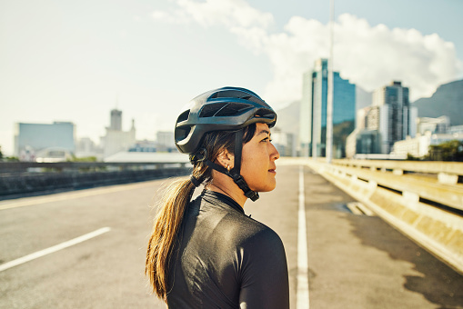 Fitness, cycling and woman with helmet, travel outdoor and bike ride in cityscape with safety and active lifestyle. Sustainable, biking and training, urban street and looking at view with mockup