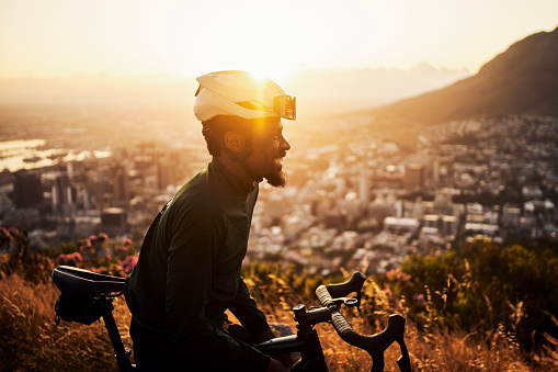 Mountain bike, sports and black man for fitness, travel or triathlon training in morning sunrise and cityscape. Adventure, nature and success of cycling person on bike and safety gear on rock journey