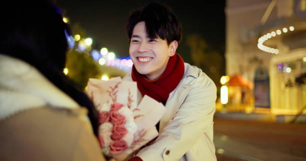 asian man is proposing to woman with bouquet at night