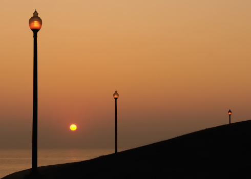 Three lamp posts are lit in front of sunrise over Lake Michigan