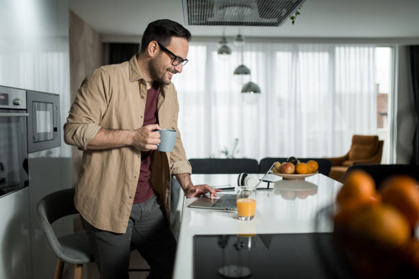 istock Happy young man using laptop while drinking his morning coffee at home. 1469633918