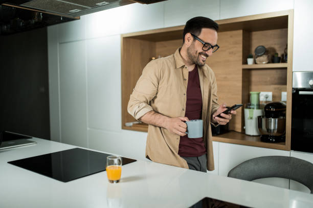 istock Happy young man using his cell phone on kitchen counter at home. 1469634616