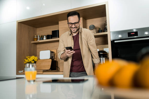 istock Happy young man using his cell phone on kitchen counter at home. 1469635628