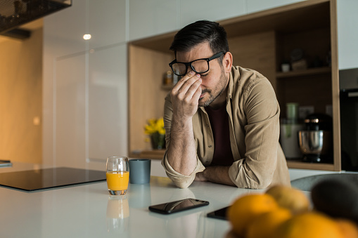 Sad young man covering his face while contemplating about his problems at home.