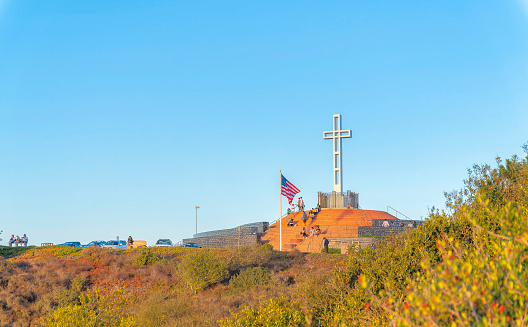 Tourists at Mount Soledad Cross in La Jolla, San Diego, California. Views of people visiting the Mt. Soledad cross on top of the mountain slope with wild green plants.