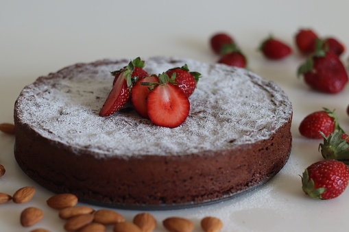 Torta caprese. Chocolate and almond cake. A yummy chocolaty flourless cake from the Capri island of Italy. Sprinkled with sugar powder and shot along with fresh strawberries on white background.