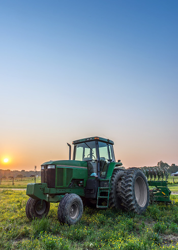 Vertical farm landscape of a tractor in a field on a farm with a setting sun in background