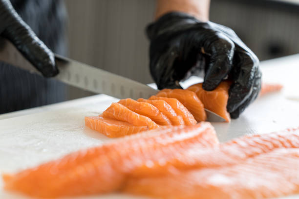 Closeup male hands slicing salmon. Chef cutting fresh fish. A worker cutting salmon on a board. stock photo
