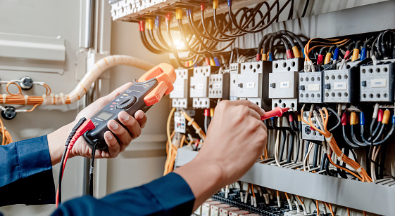 El ingeniero electricista utiliza un multímetro para probar la instalación eléctrica y la corriente de la línea de alimentación en un armario de control del sistema eléctrico. photo