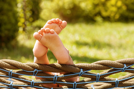 Happy Vacation on Nature. Child barefoot on hammock on greenery background. Happy Holiday Childhood Concept.