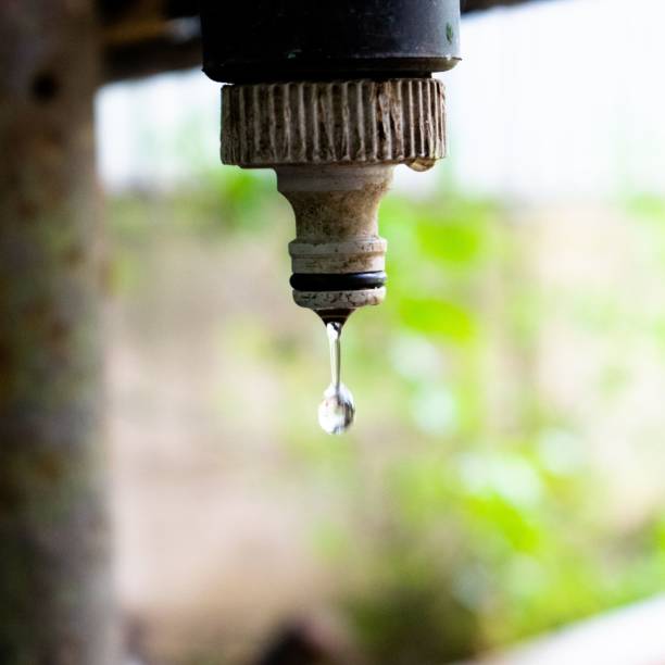 istock Water drop dripping from a metal pipe with blurred green background 1469662501