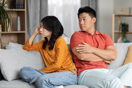 Divorce, relationship crisis, marriage and conflicts concept. Upset asian couple sitting on couch at home, unhappy chinese man and woman in homewear having quarrel, dont talk to each other