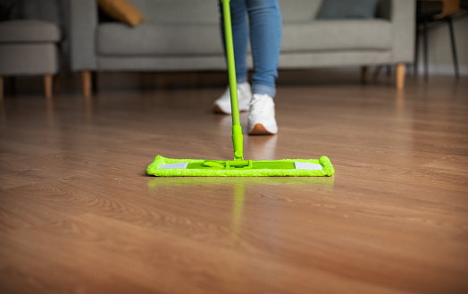 Unrecognizable Woman Mopping Floor With Mop Standing In Modern Living Room At Home. Cropped Shot Of Lady Cleaning House And Doing Chores. Housework Concept. Selective Focus