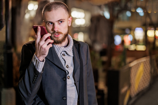 Handsome Man is Walking in the City Streets and Talking over the Smart Phone During an Autumn Night in the City.