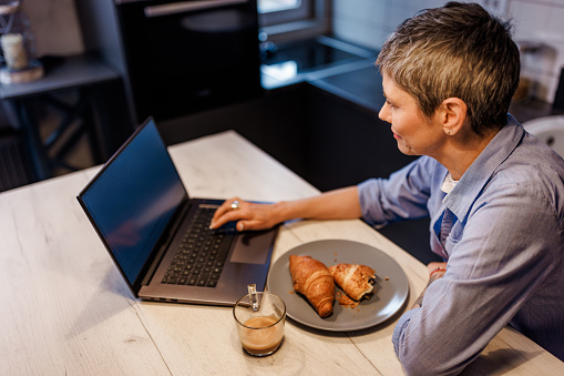 Mature woman using laptop during breakfast at home