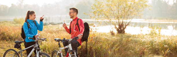 istock Young Caucasian couple eating energy bars and talking while taking a break from a mountain bike ride by the river 1469672836