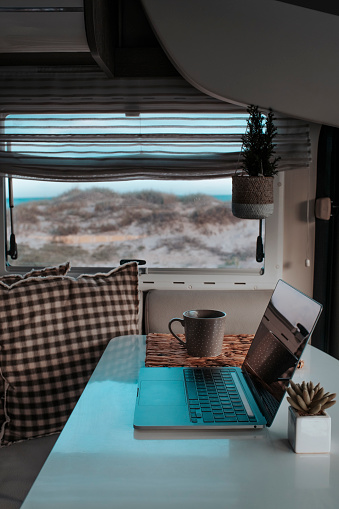 Vertical image of digital nomad smart working freedom alternative office vanlife lifestyle concept. One laptop computer on the dinette table of a camper van. Modern vacation and business job