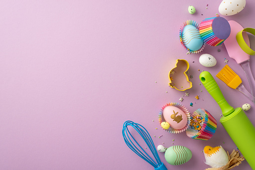 Easter concept. Top view photo of kitchen utensils whisk rolling pin silicone spatula brush colorful easter eggs in paper baking molds chicken and sprinkles on isolated lilac background with copyspace